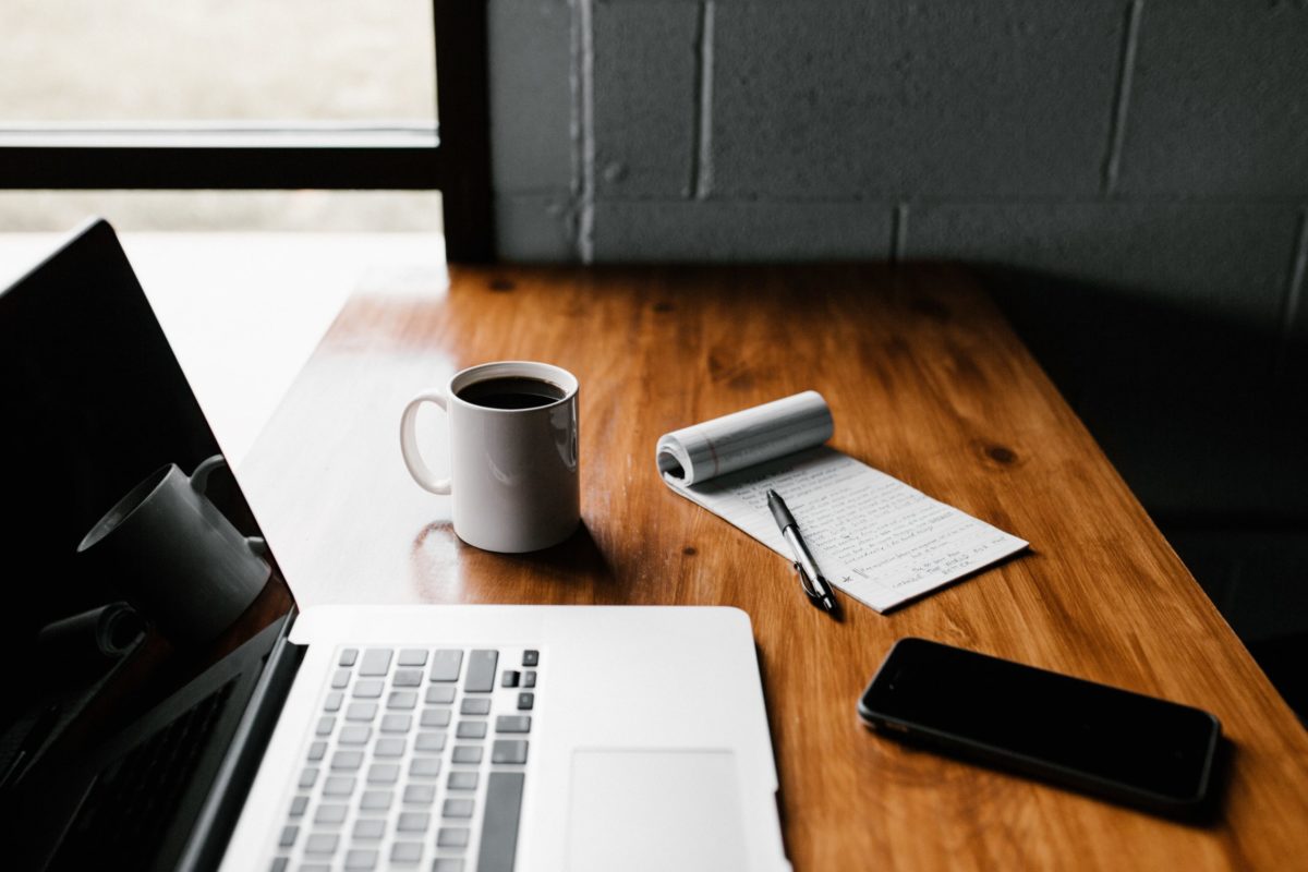A desk with a laptop, phone, coffee, pen, and paper on it